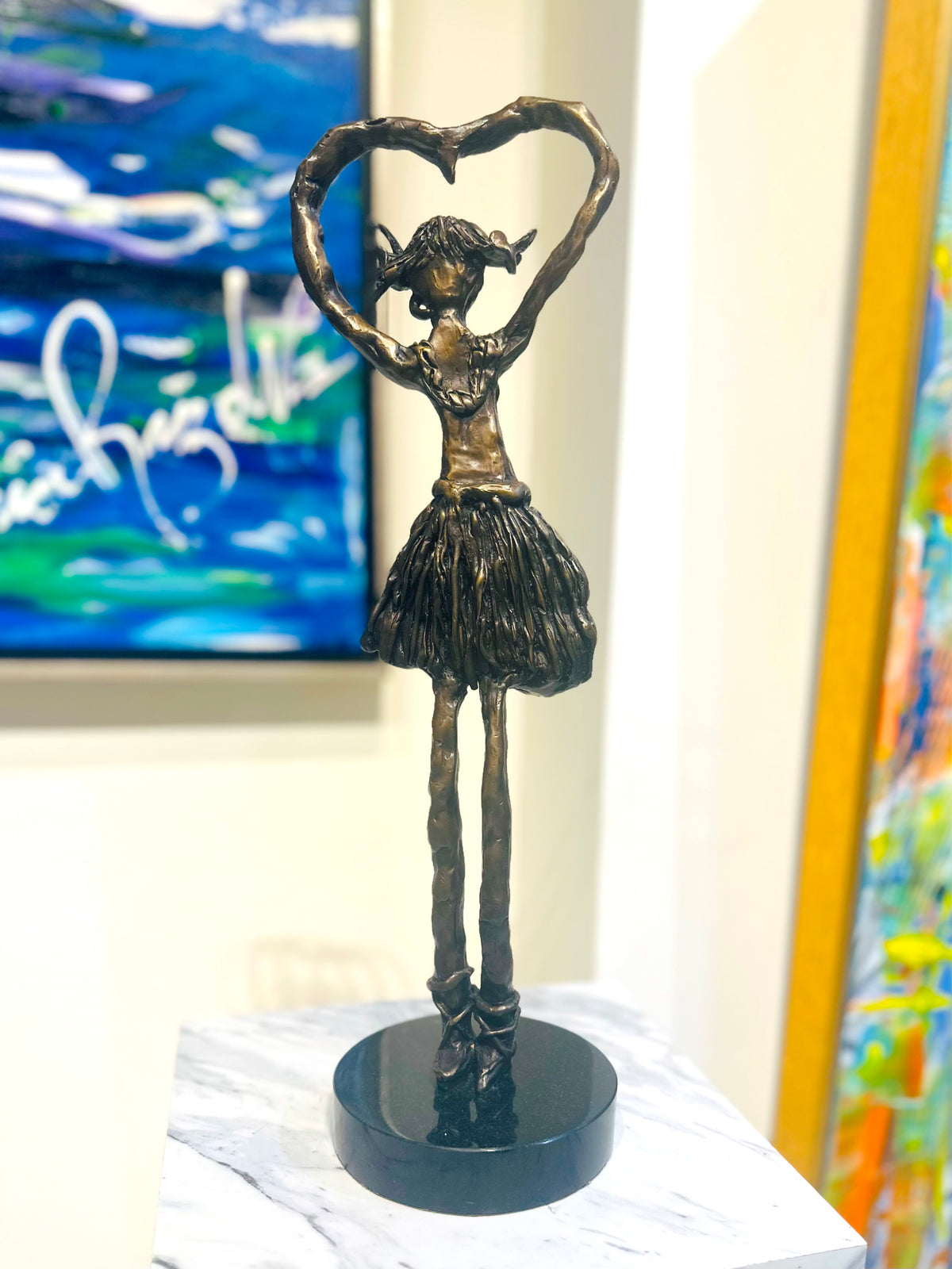 Ashleigh — bronze sculpture by Veronica Ruiz de Velasco. A bronze figure of a young girl on tall, narrow legs with her arms lifted to form a heart above her head.